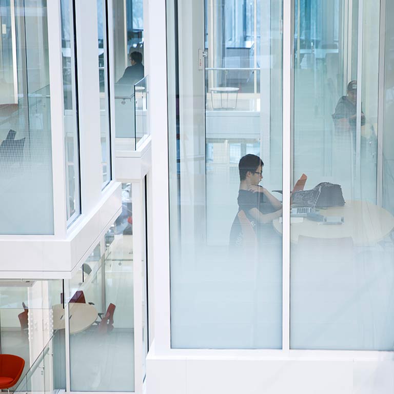 A student sits in a transparent room in Luddy Hall, while other rooms are visible behind him.