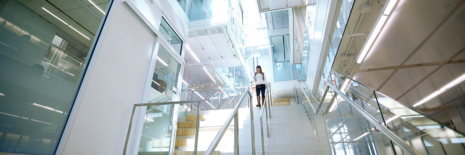 A student walks down the stairwell and listens to music from her phone in the Luddy Hall atrium.