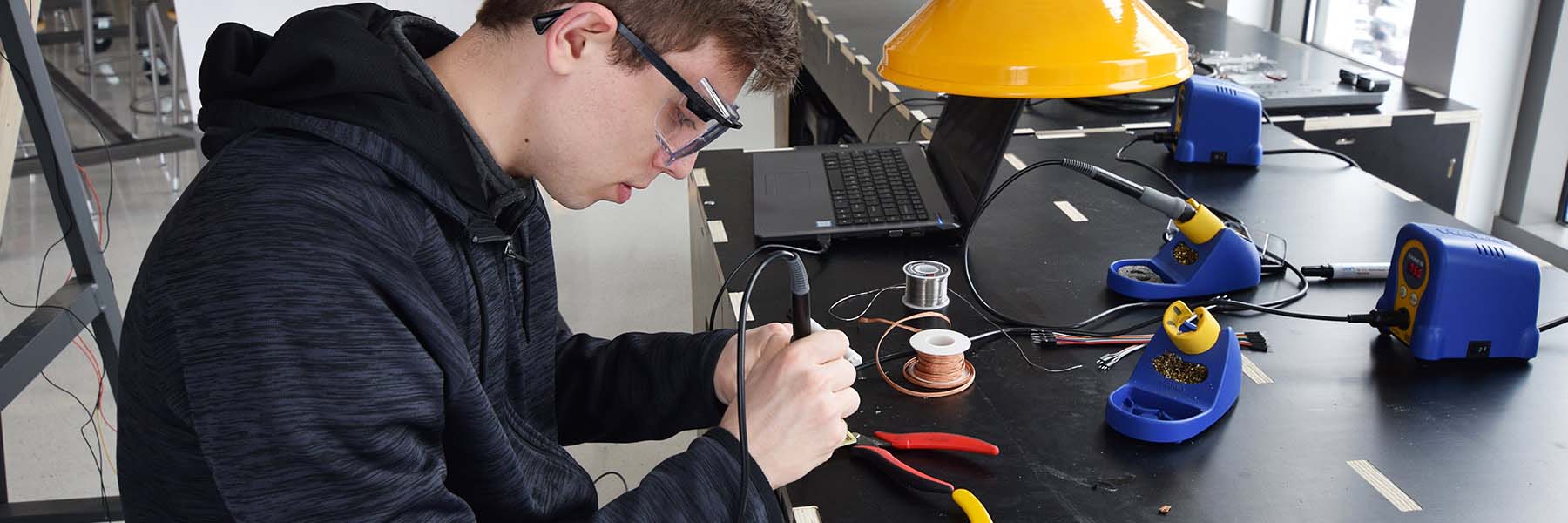 A student wearing goggles solders electronic hardware in a makerspace in Luddy Hall.