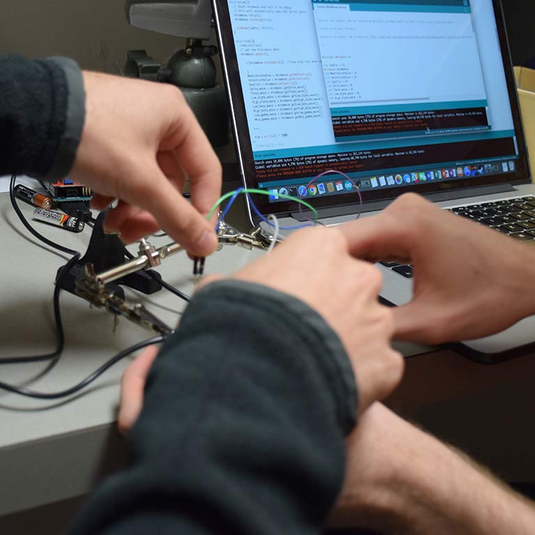 A close-up of two students' hands as they put wires on an electronic device