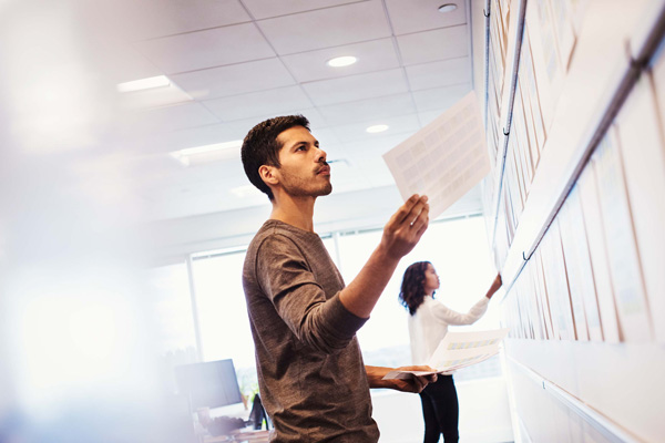 two students in a classroom standing in front of wall of papers looking at them.