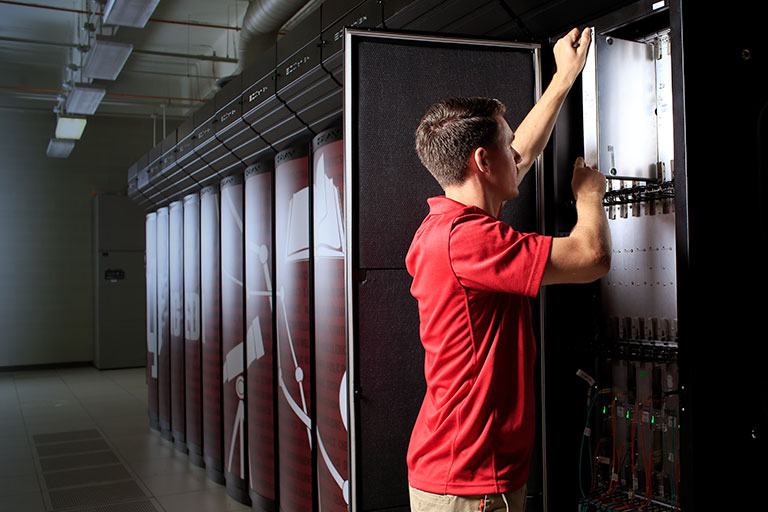 A male inserts a piece of equipment into a supercomputer. 